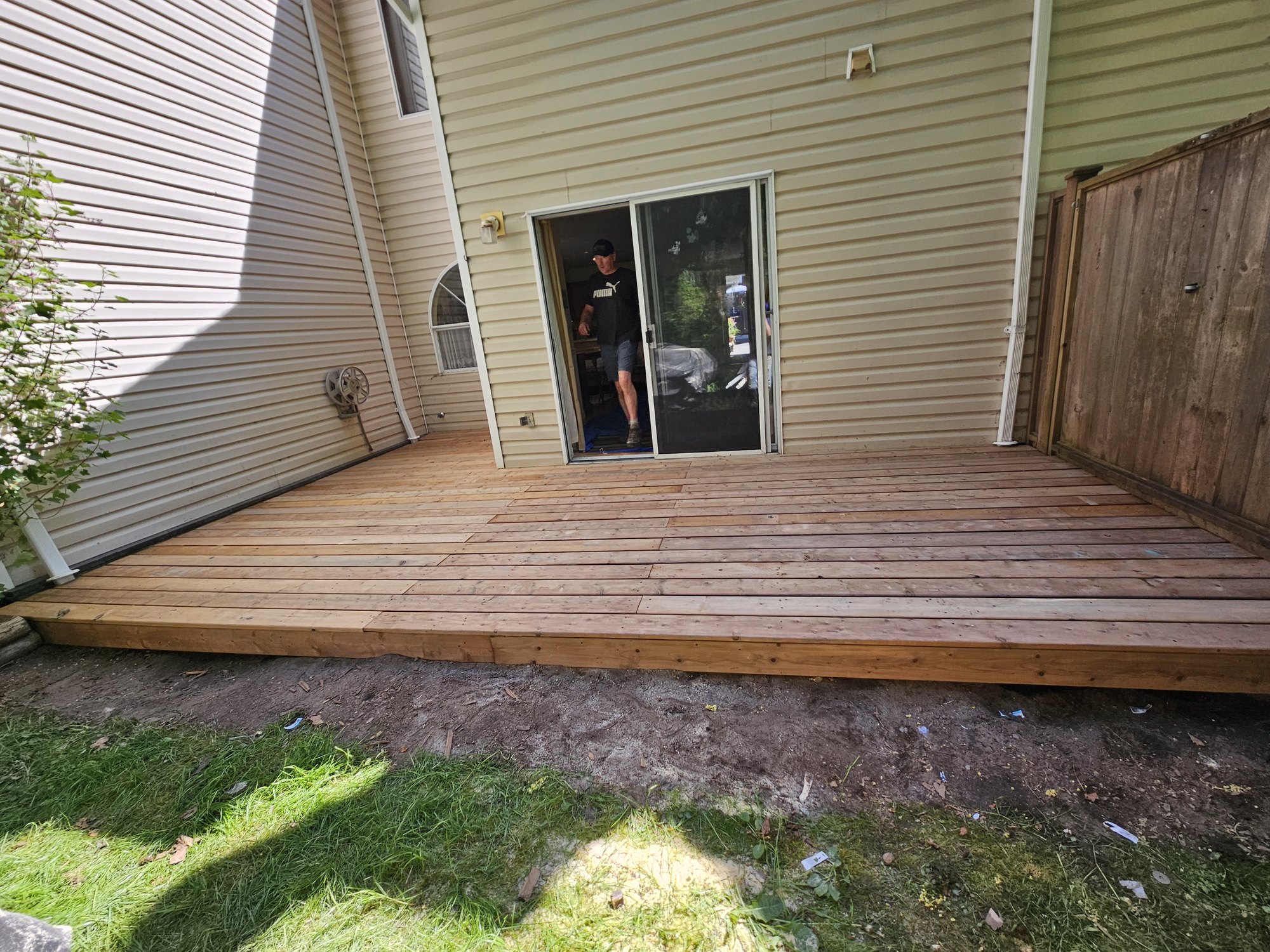 A newly built low-profile cedar deck against the back of a Peninsula home, running out to a sliding patio door