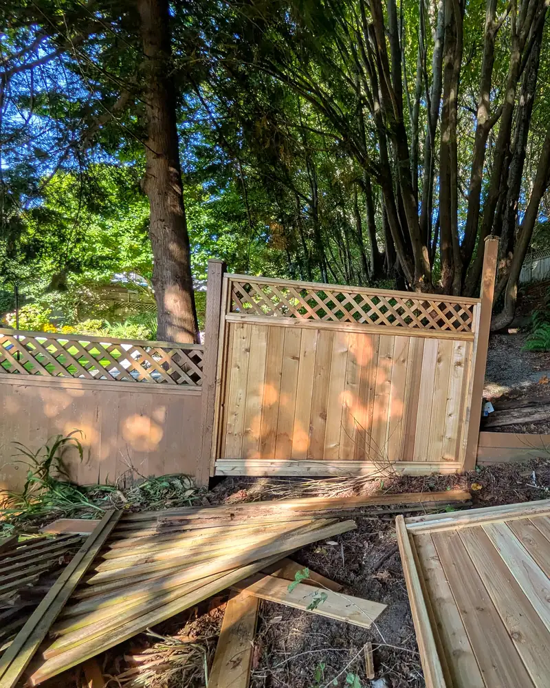 Mid-job: the new cedar panel set in place, with the old boards torn out on the ground and a prefab cedar panel ready